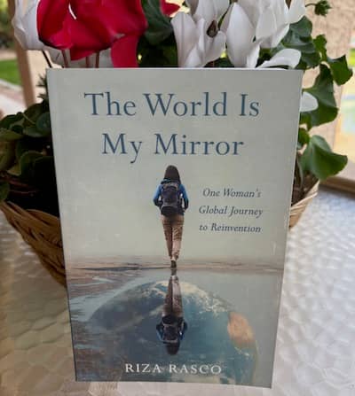 Photo of Riza Rasco’s memoir, The World Is My Mirror, against a backdrop of flowers