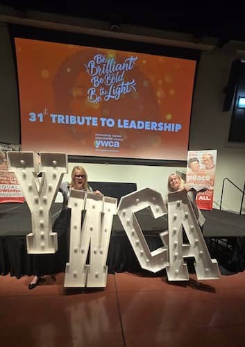 Stacey Gualandi (left) and Pam Burke on stage at the YWCA Tribute to Leadership event in Phoenix, AZ, holdng up the big letters YWCA 