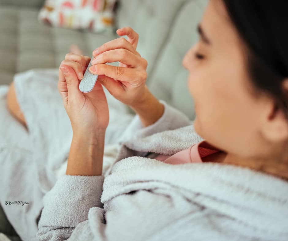 Woman in a robe on a couch filing her nails