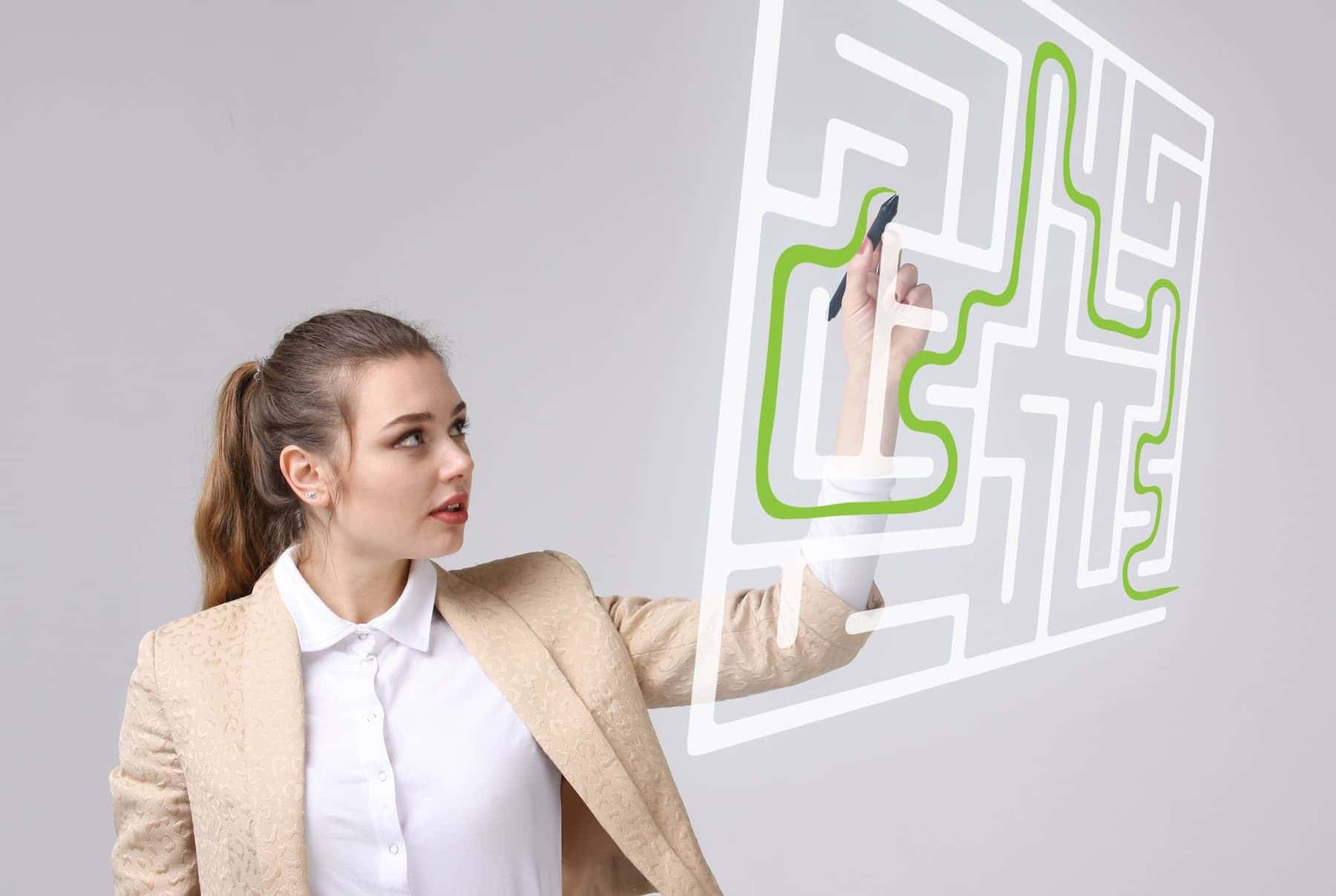 Woman in beige jacket drawing a green path through a maze on a transparent screen, symbolizing a growth mindset brain solving challenges.