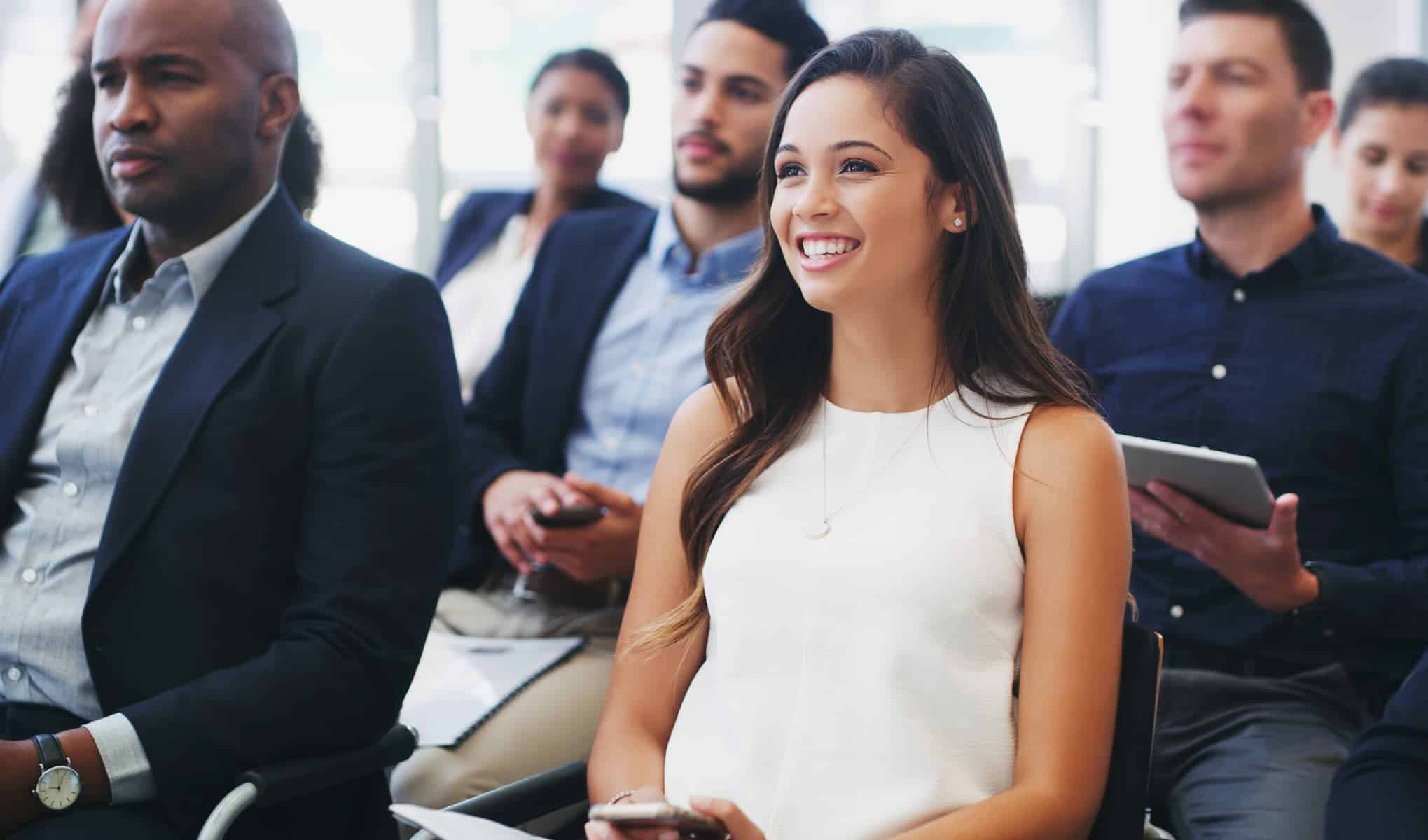 A woman in a white dress sits at a seminar, listening attentively and resolutely determined to succeed by ignoring the naysayers.