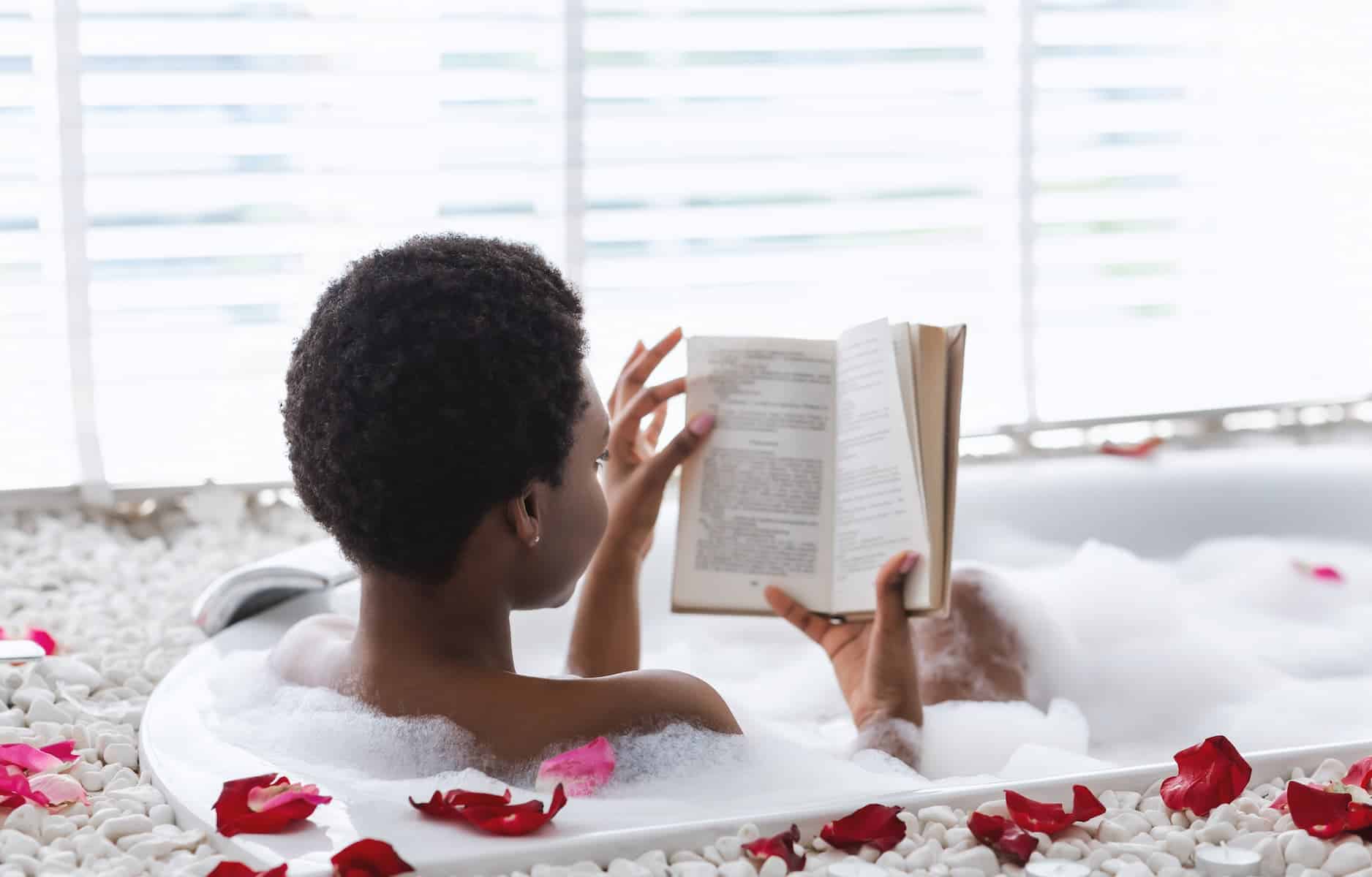 A calm woman reads in a petal-filled bubble bath, capturing a soothing scene that can blur into negative self care when used to escape emotions.