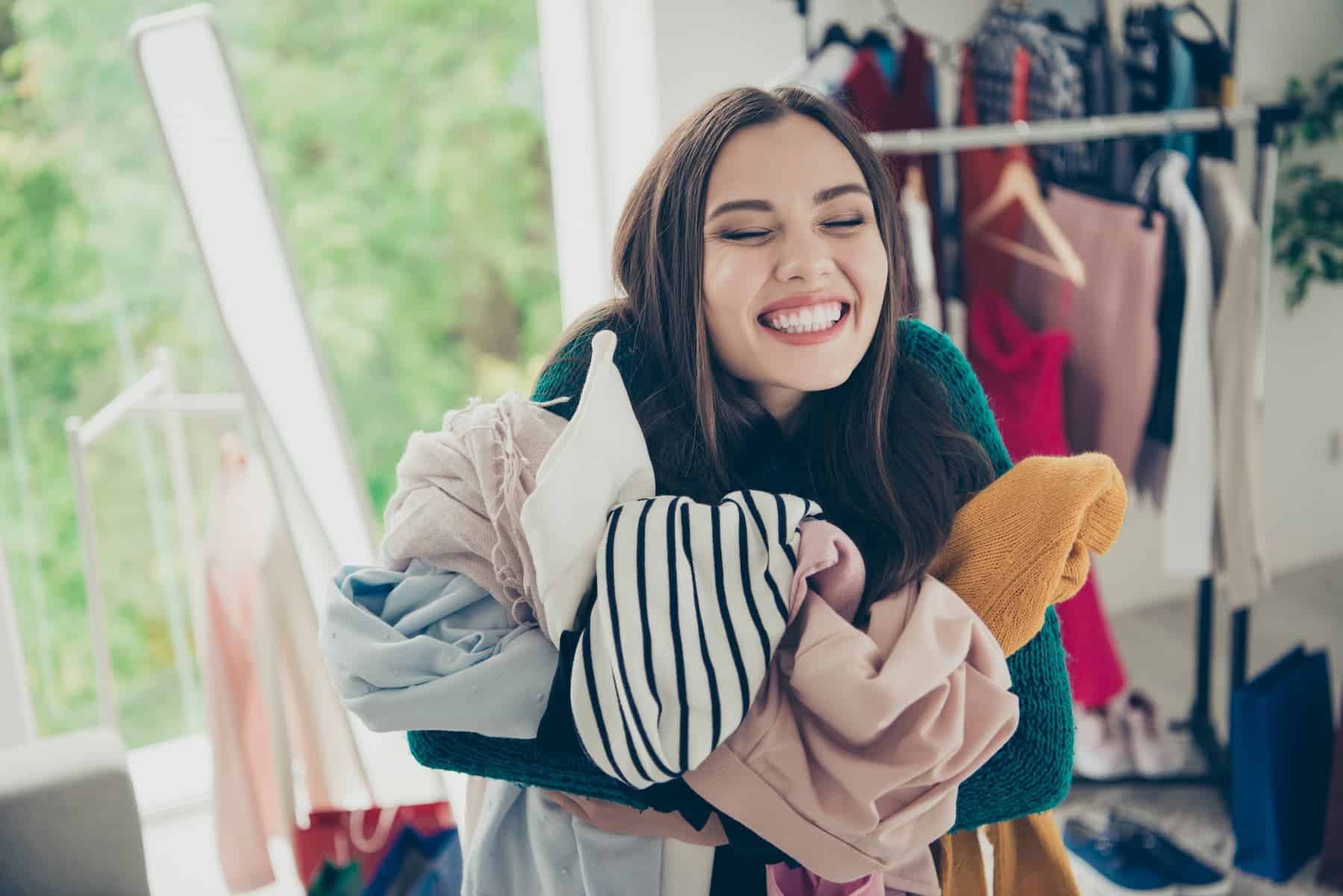 A happy young woman hugs her clothes tightly, showing a strong attachment to material things and a reluctance to let go of her possessions.
