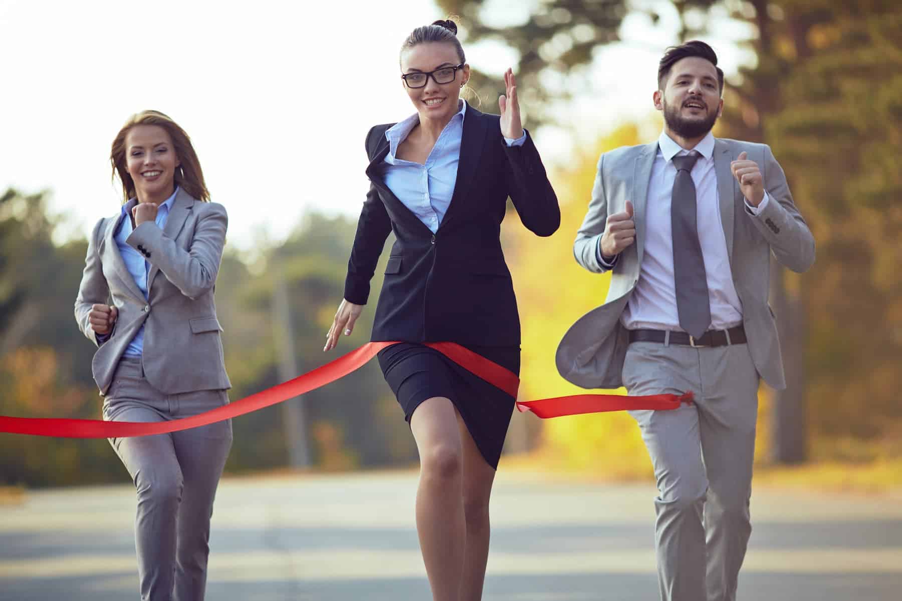 A businesswoman in glasses crosses the red ribbon, finishing first in a race against two colleagues — a powerful image of her journey from victim to victor.
