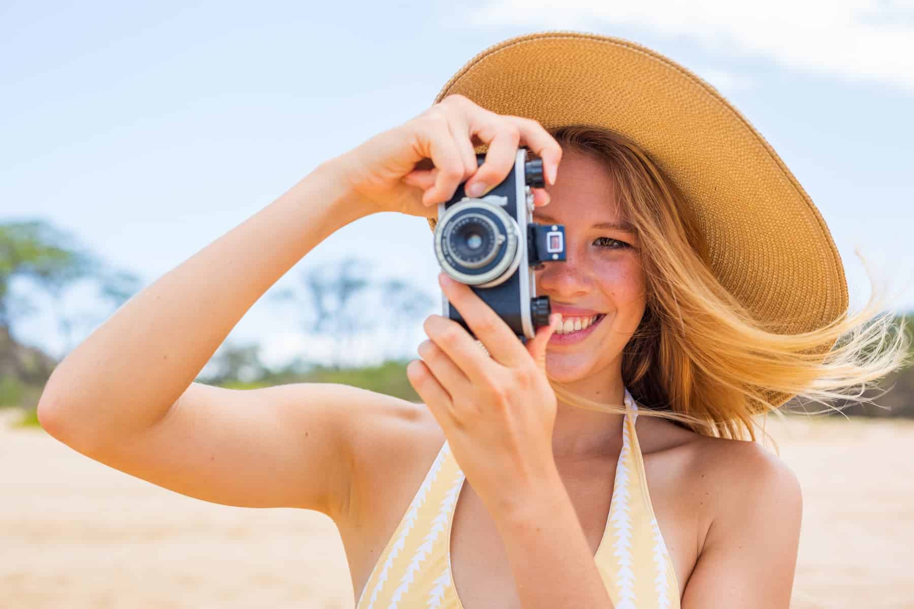 A woman taking photos on the beach with a vintage camera, highlighting photography as one of the creative hobbies to try.