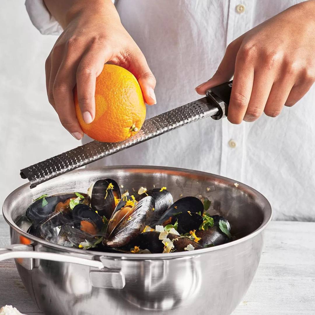 Hand using a microplane zester to zest orange over a bowl. 