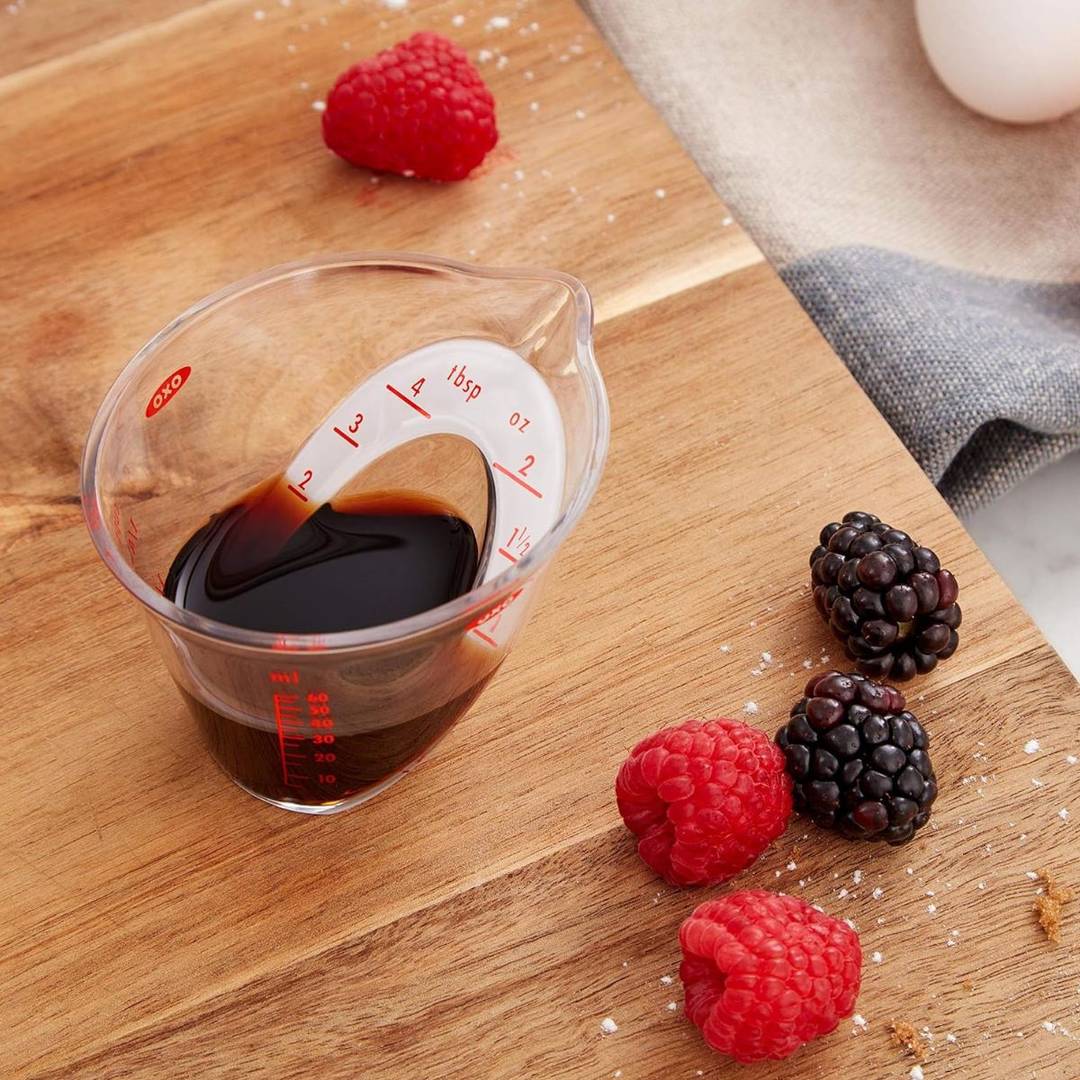 A mini oxo measuring cup on a cutting board with berries. 