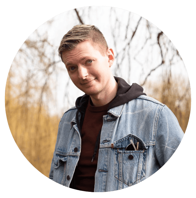 An image of Zach! He's wearing a black hoodie under a denim jacket, standing outside in front of some autumnal trees