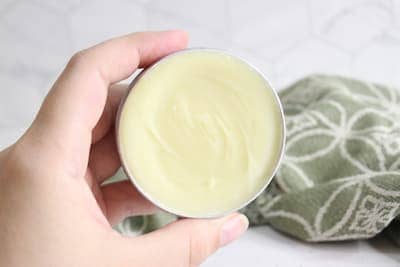 a tin of homemade natural deodorant cream being held by a woman's hand