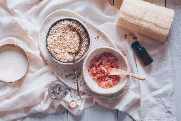 bowls of ingredients for a body scrub, and a bottle of essential oil
