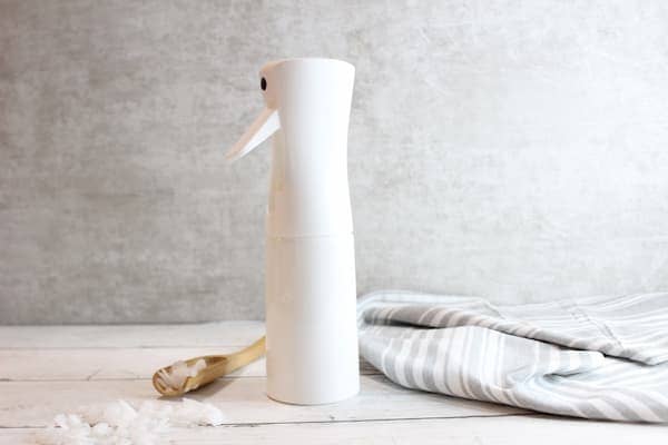 a spray bottle of homemade magnesium spray and a spoon with dried magnesium flakes