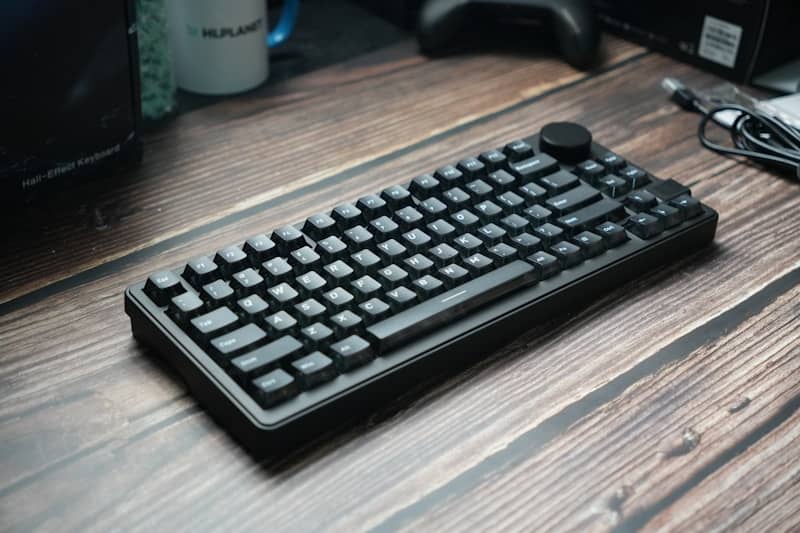 A black mechanical keyboard rests on a wooden desk.