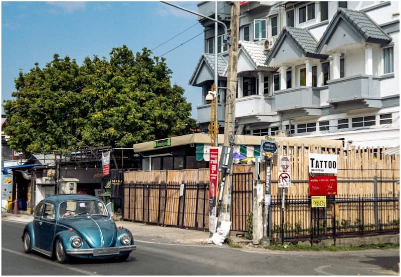 A blue volkswagen beetle drives down a street.