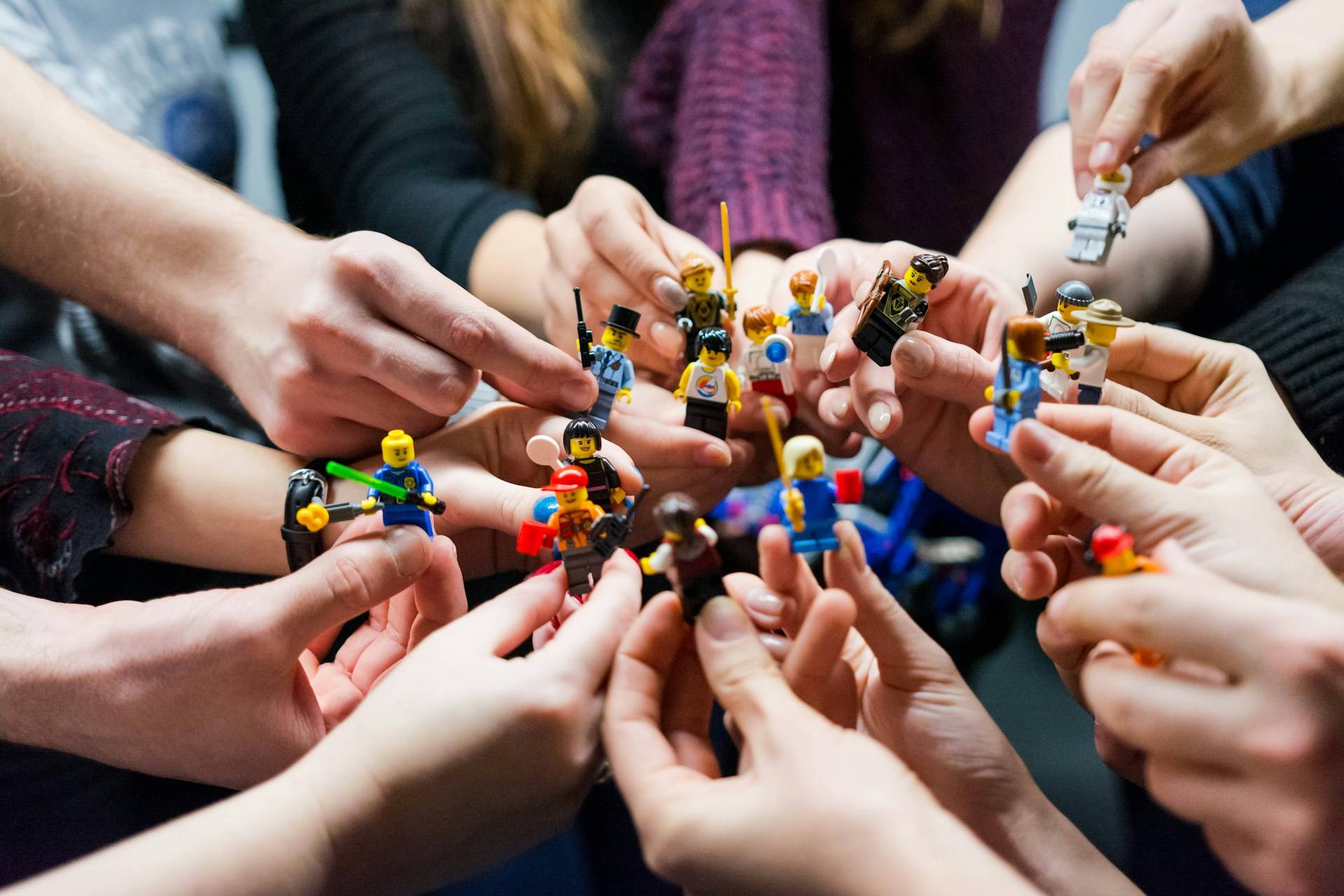 Many hands extended into the center, each holding a different LEGO figure