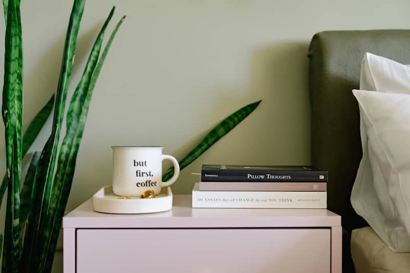 A nightstand displays books, a mug, and a plant.