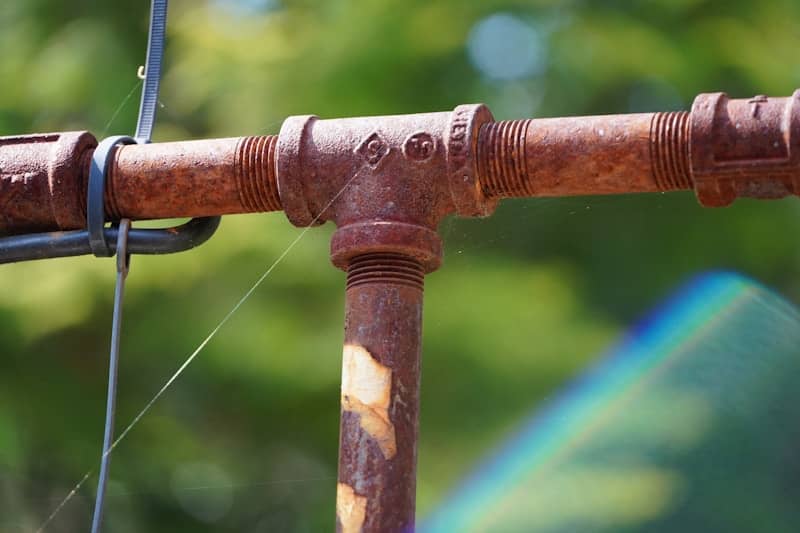 Rusty metal pipes are connected together in a t shape.
