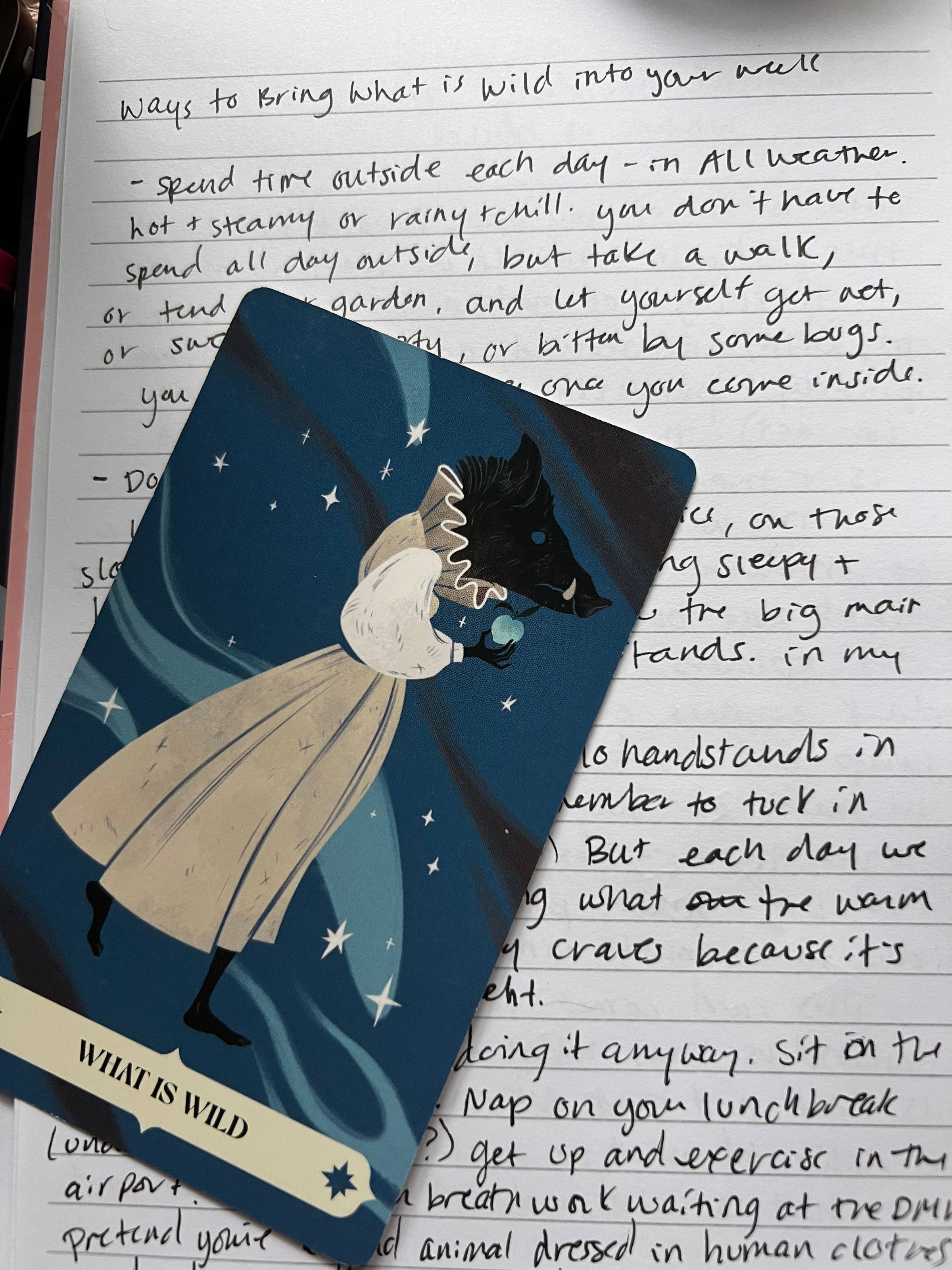 an oracle card with a wild boar wearing a dress and holding an apple lays on top of a page of handwritten notes