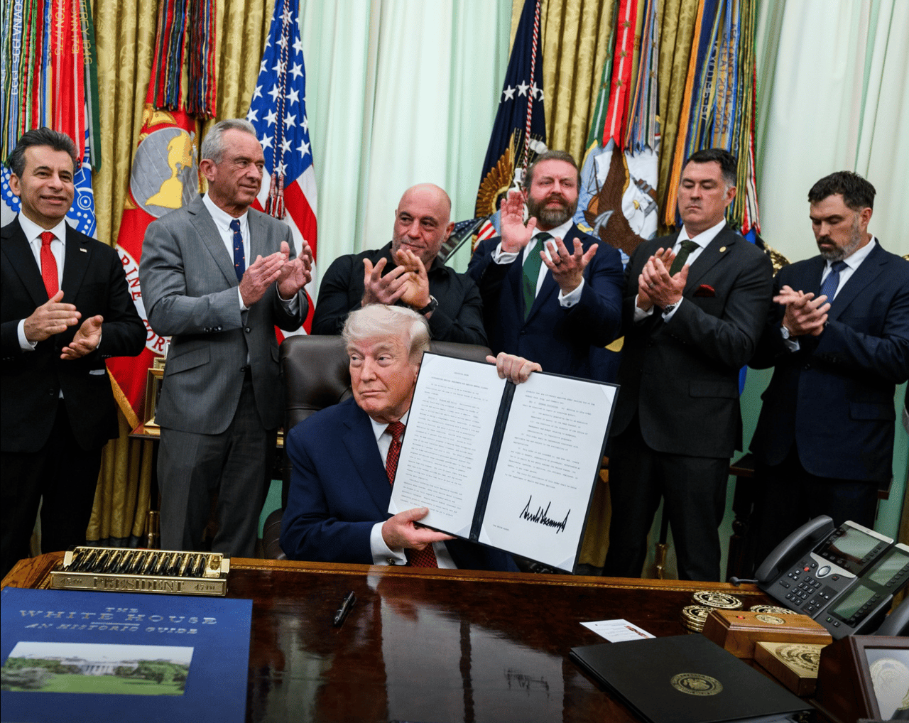 President Donald Trump holds up the signed executive order flanked by a group of men.