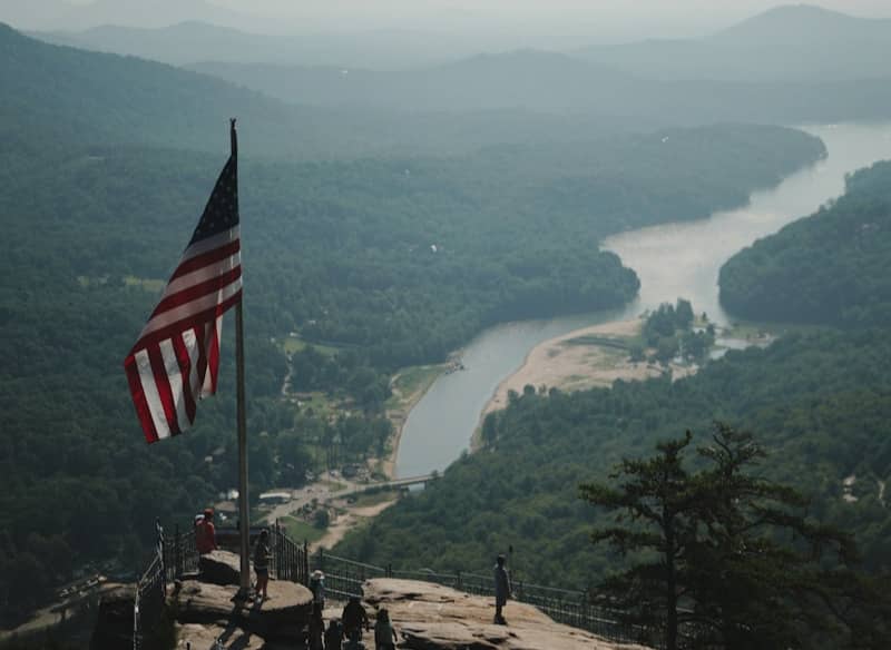 American flag on a mountain peak overlooking a river valley.
