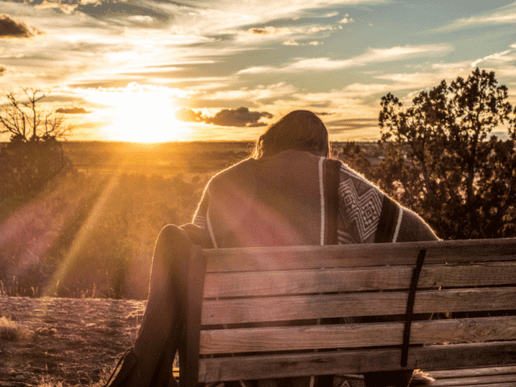 woman sitting outside leaning over as the sun rises