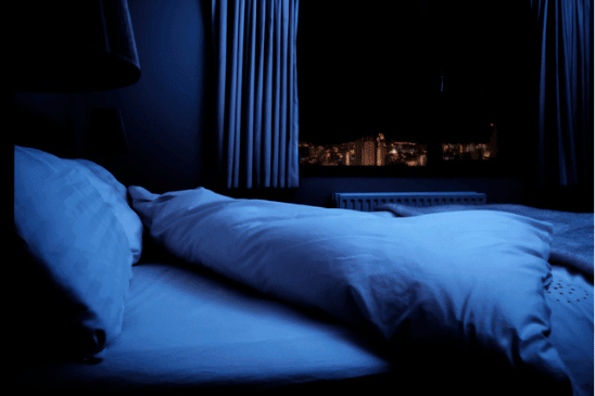 a bed in front of an open window with a view of the evening sky