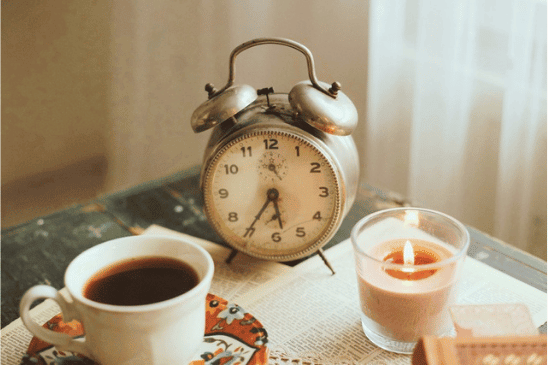 a clock with a cup of coffee, a candle and a book