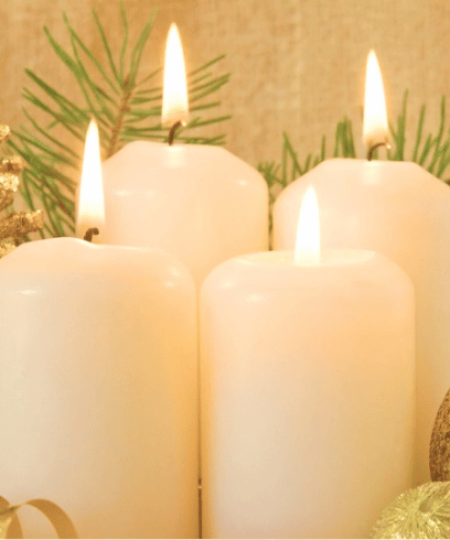 white candles lit with green shrubbery in the background
