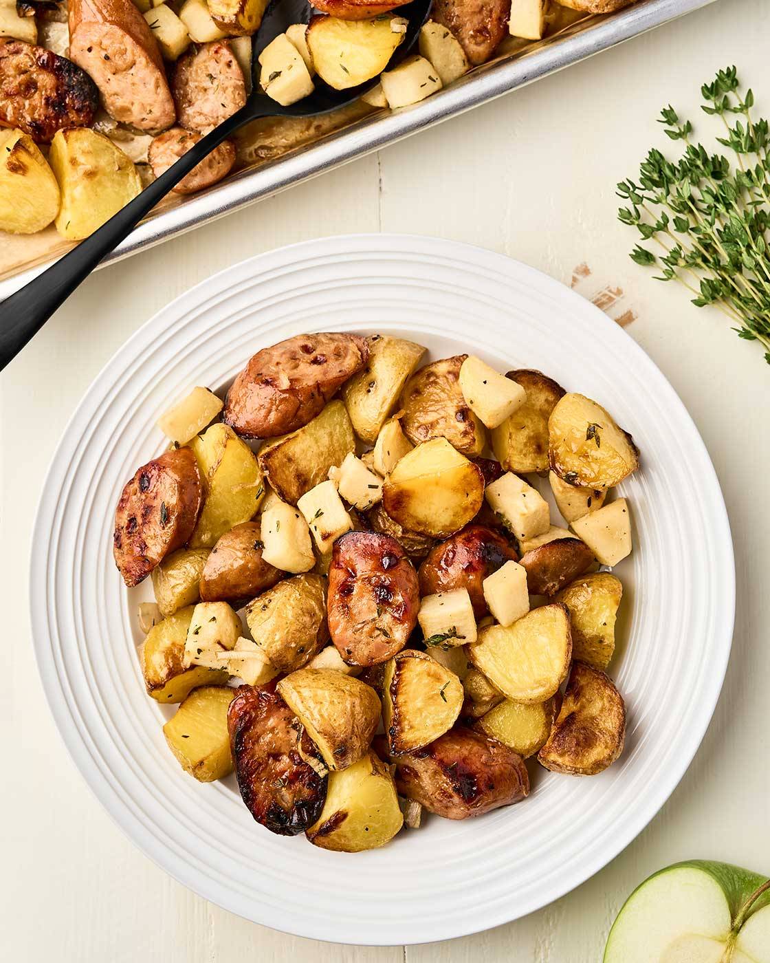 Roasted chicken sausage with apples and potatoes served on a white plate.