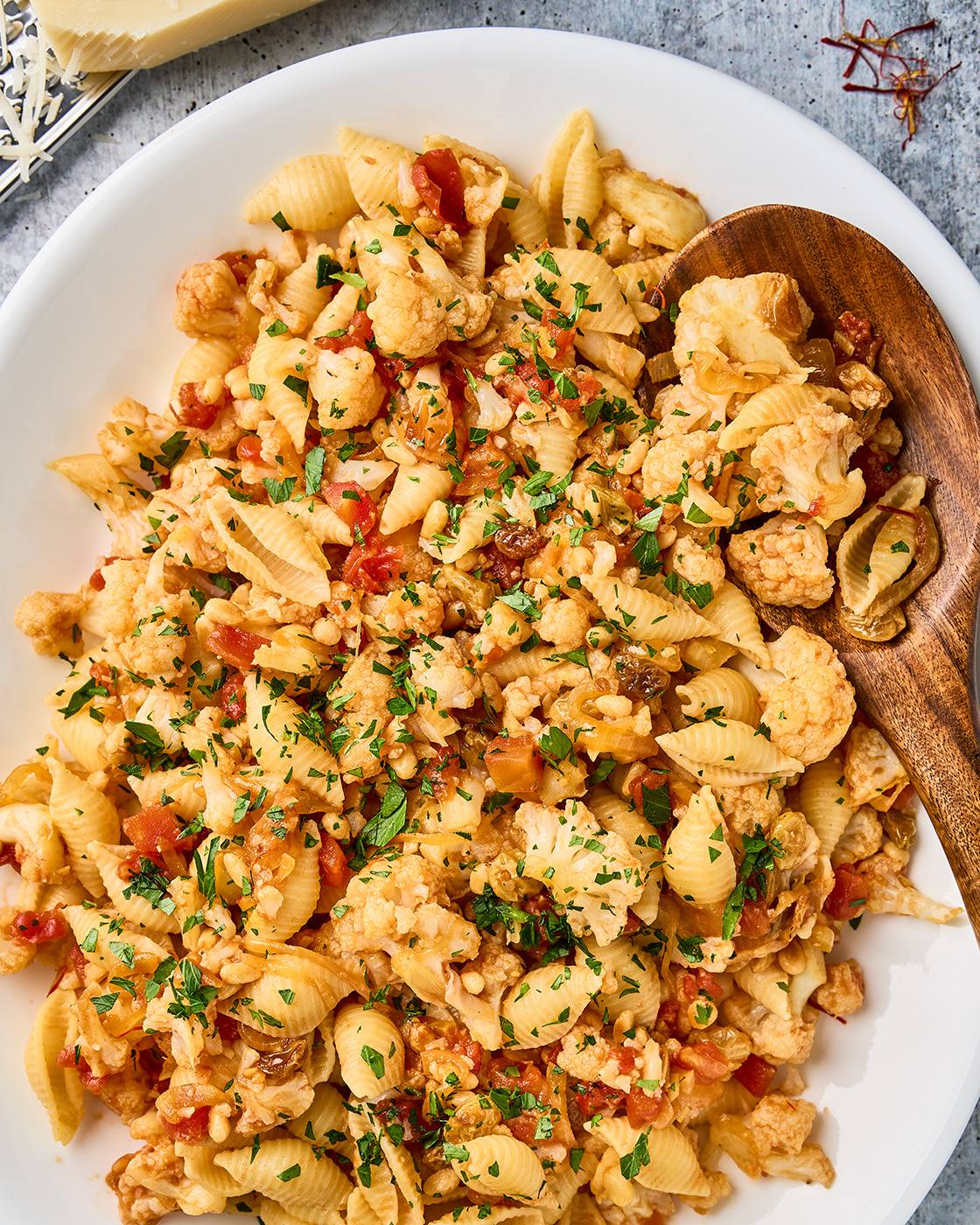 Sicilian pasta with cauliflower, shell pasta, tomatoes, raisins, pine nuts, and chopped parsley on a white platter.