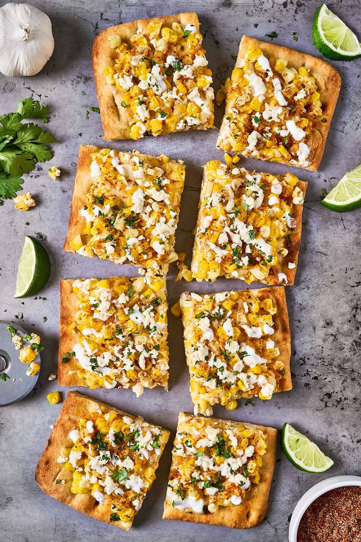 Mexican street corn flatbread cut into pieces on a baking sheet and garnished with fresh cilantro and lime.
