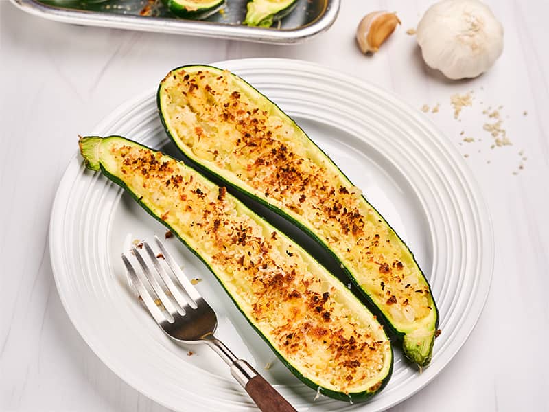 Two zucchini boats filled with caramelized onions, cheese, and panko crumbs, baked until golden brown.