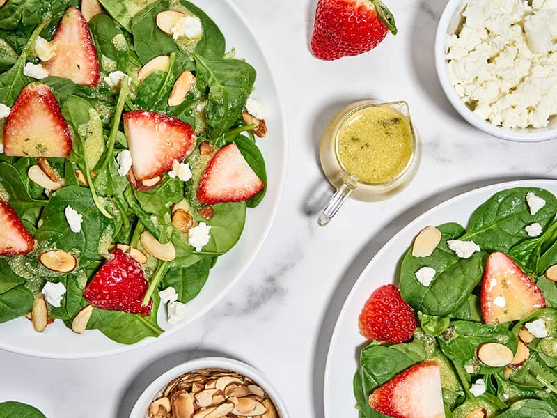 Plated spinach and strawberry salad with creamy basil balsamic dressing, goat cheese crumbles, and toasted almonds.