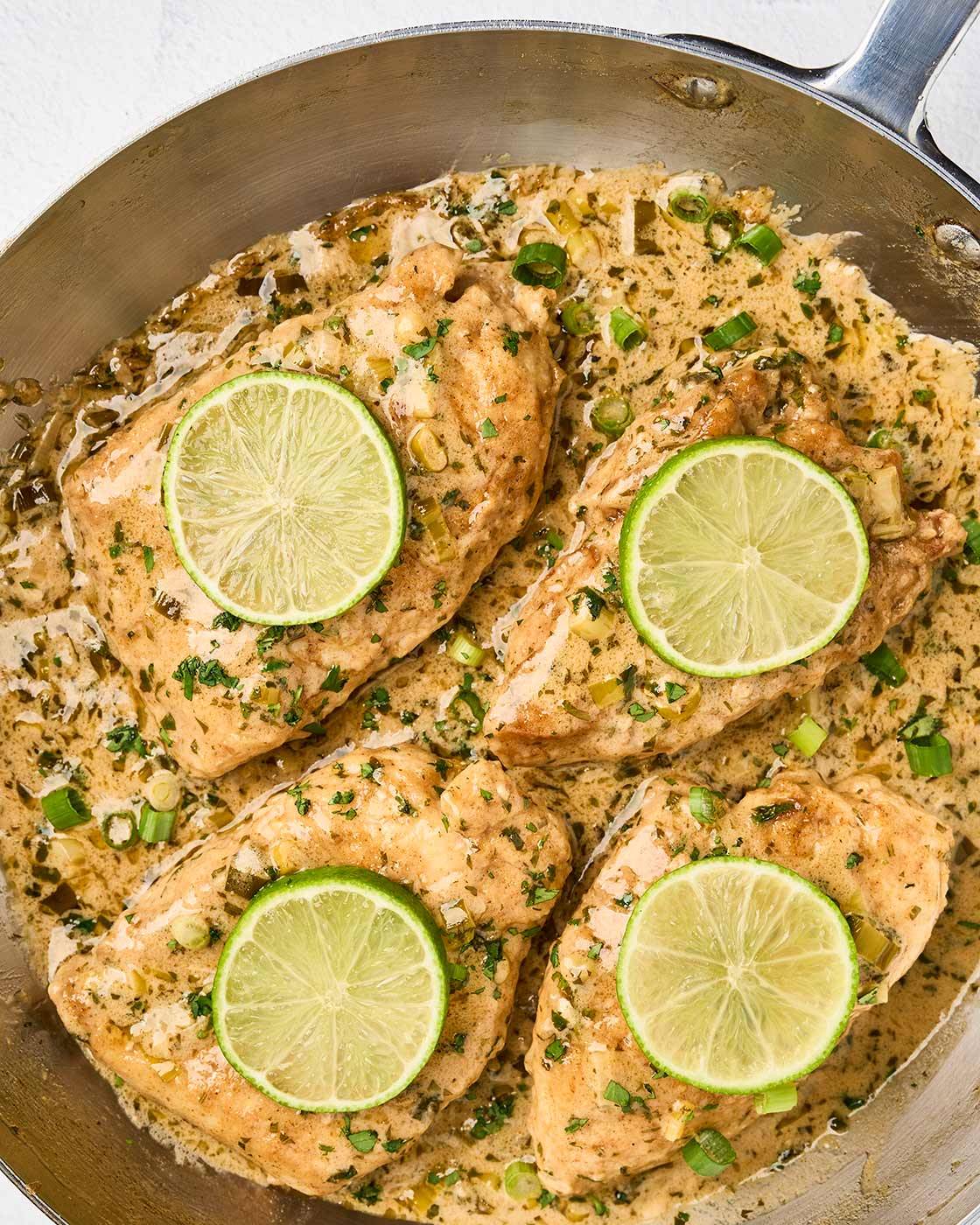Creamy cilantro lime chicken in a skillet with fresh lime slices, scallions, and cilantro garnish.