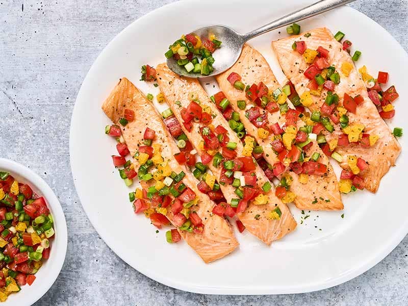 Roasted salmon with fresh orange and tomato salsa arranged on a large white platter with extra salsa alongside.
