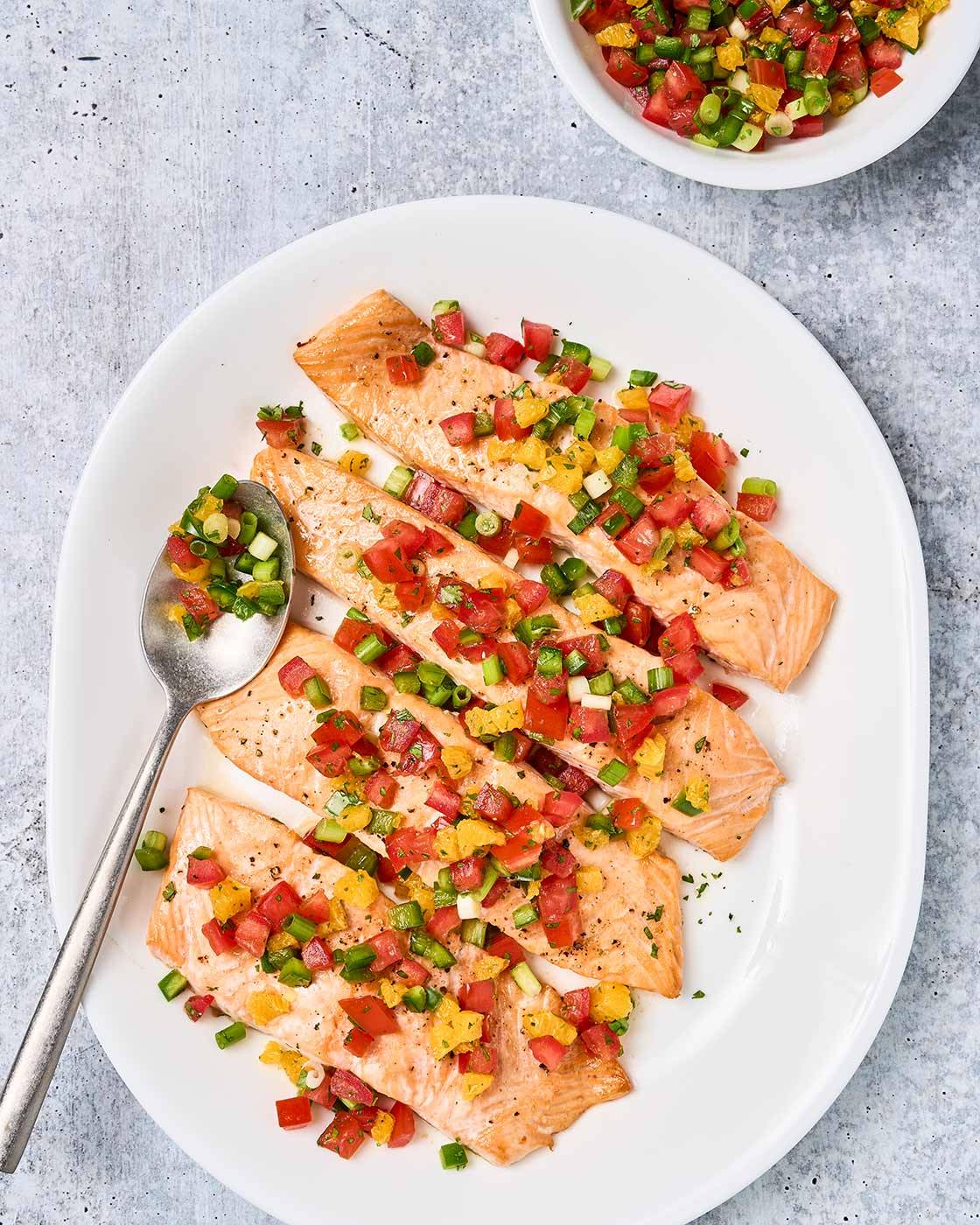Roasted salmon with fresh orange and tomato salsa arranged on a large white platter with extra salsa alongside.