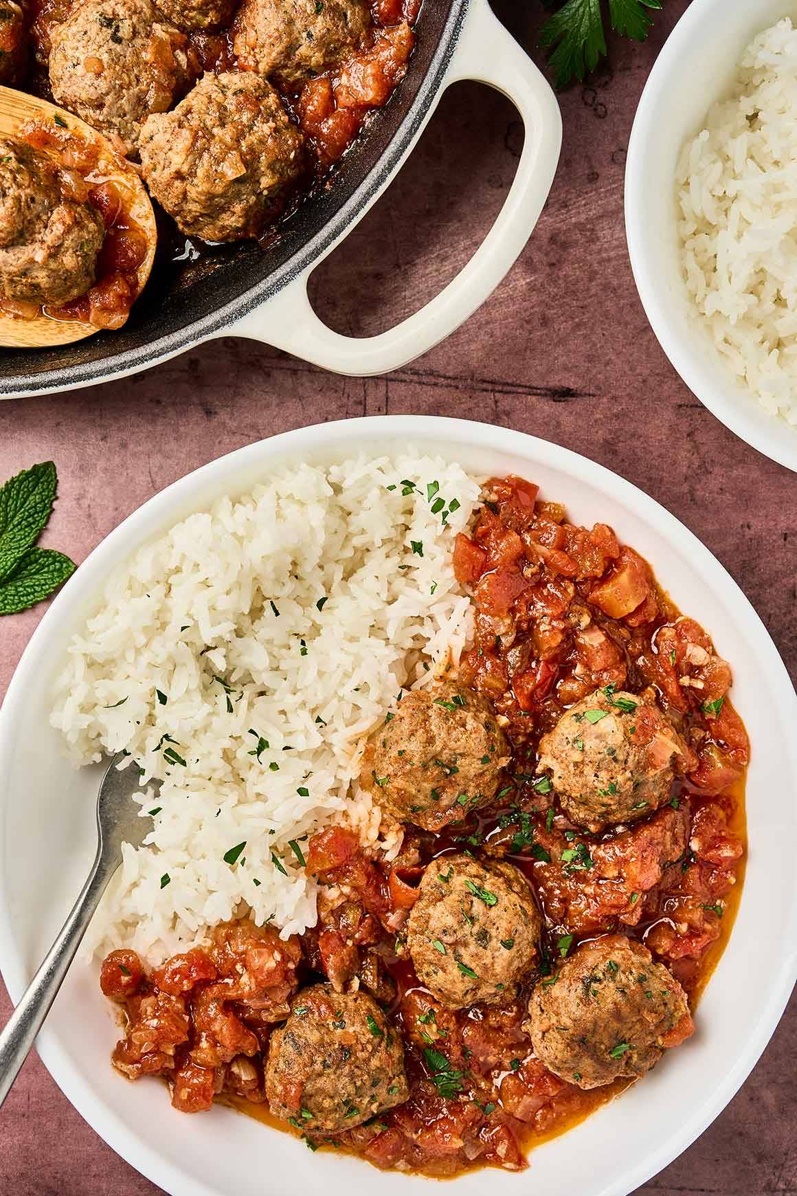 Moroccan meatballs in tomato sauce served over white rice on a plate, with extra meatballs in a skillet and fresh herbs garnish.