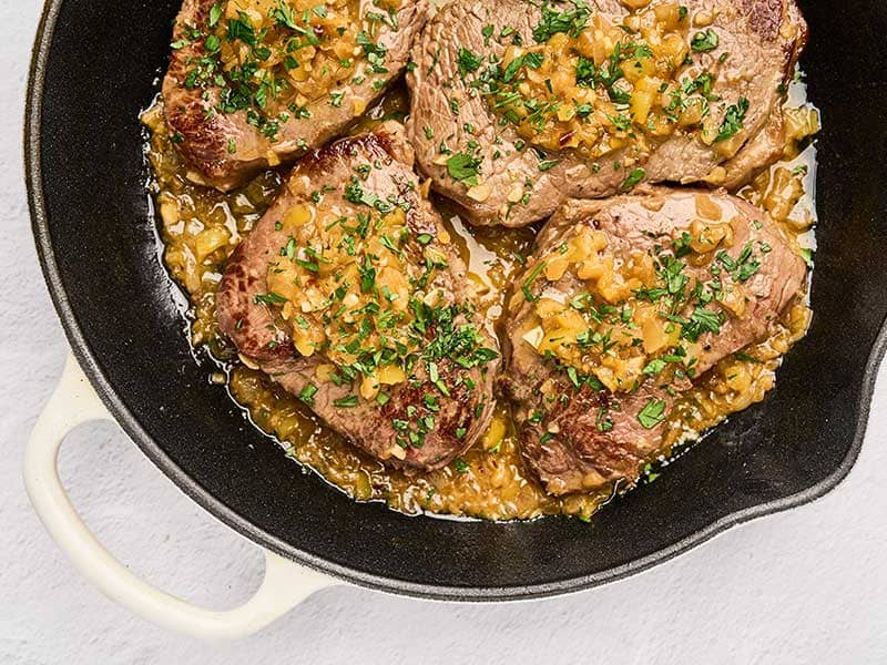 Pan-seared sirloin steaks with sautéed banana peppers and garlic butter in a skillet, garnished with parsley.