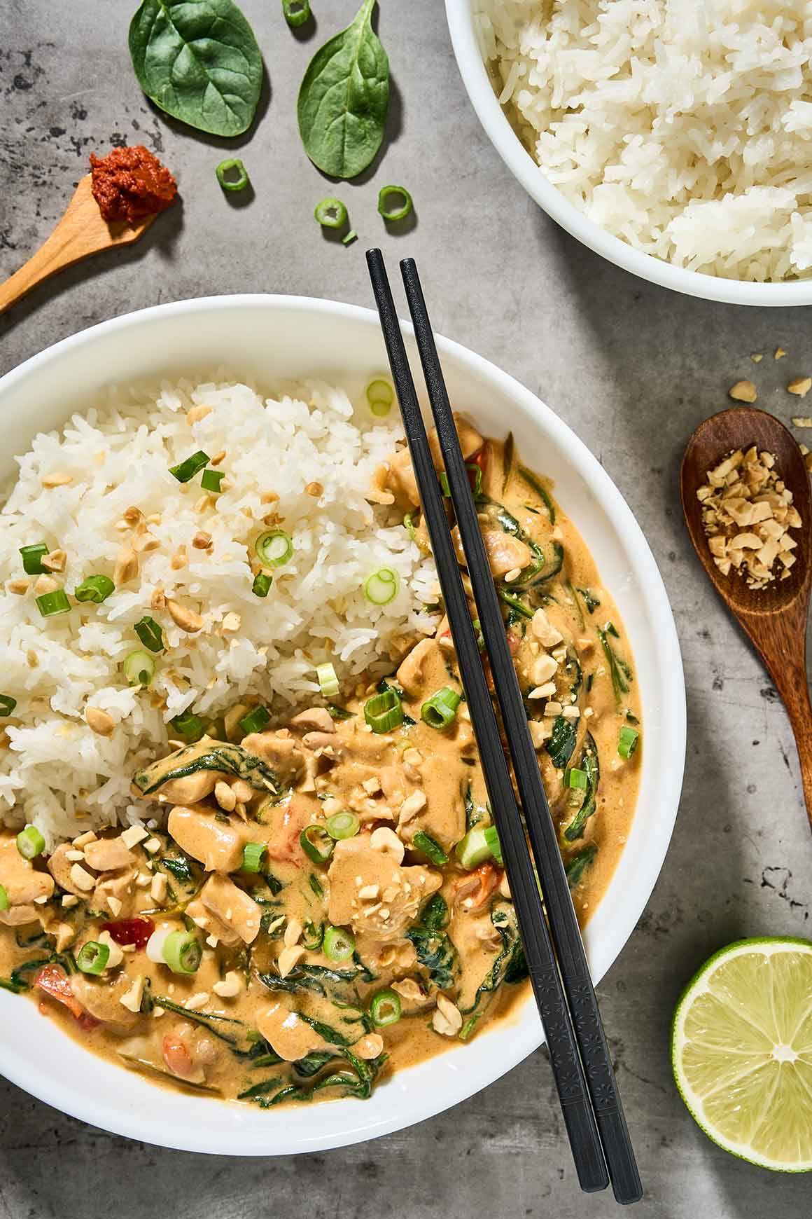 Thai peanut curry with chicken, spinach, jasmine rice, scallions, and chopped peanuts in a white bowl.