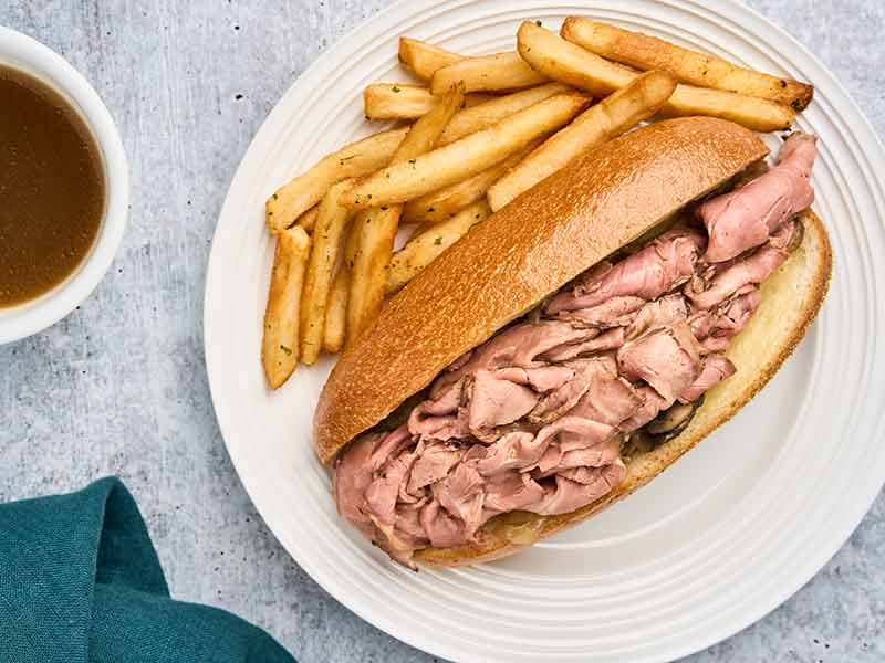 French dip sandwich with deli roast beef on a toasted roll, served with French fries and beef jus for dipping.