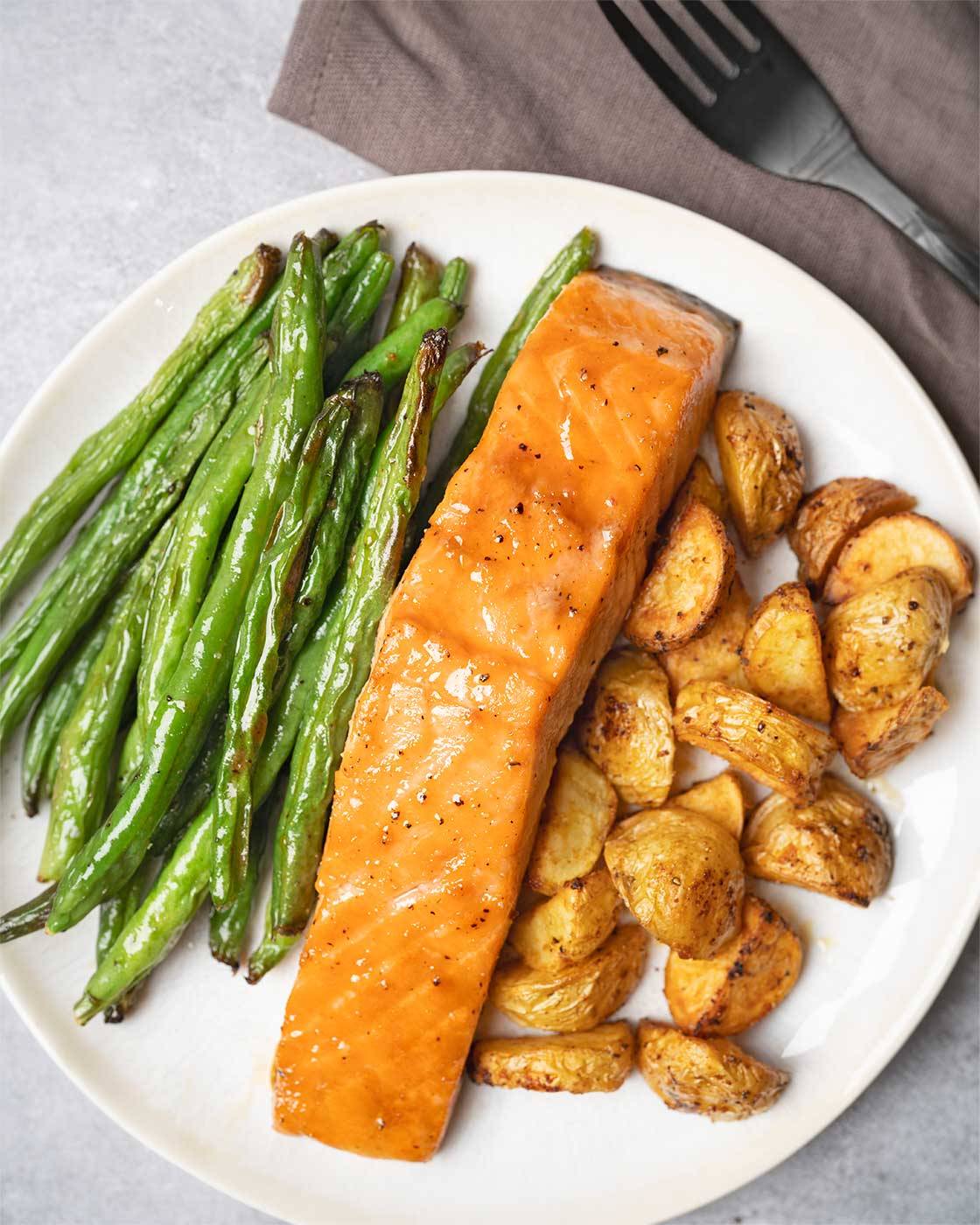 A single serving of sheet pan salmon dinner including brown sugar-glazed salmon, roasted baby potatoes, and green beans.