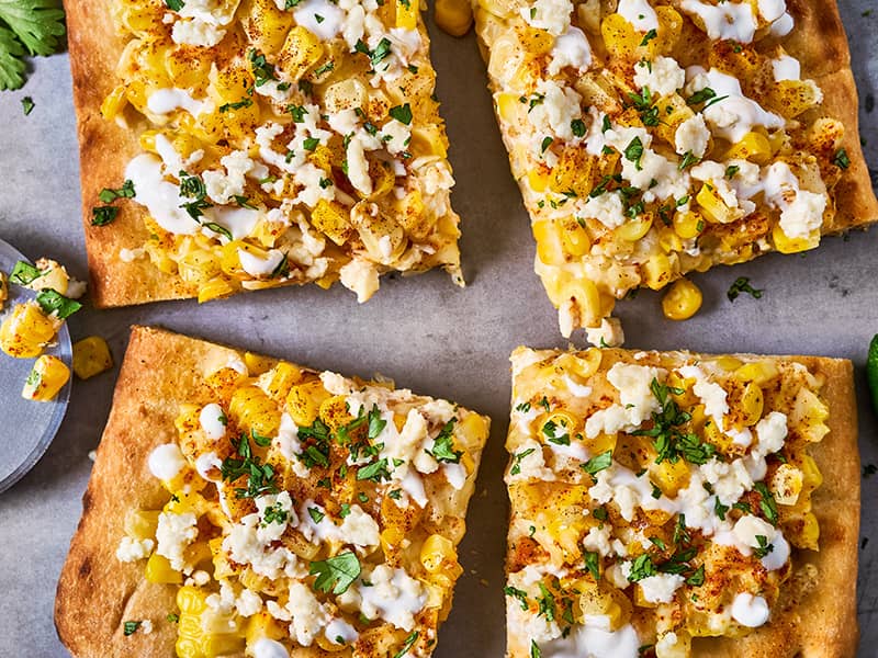 Four pieces of Mexican street corn flatbread drizzled with crema and sprinkled with queso freso and fresh cilantro.