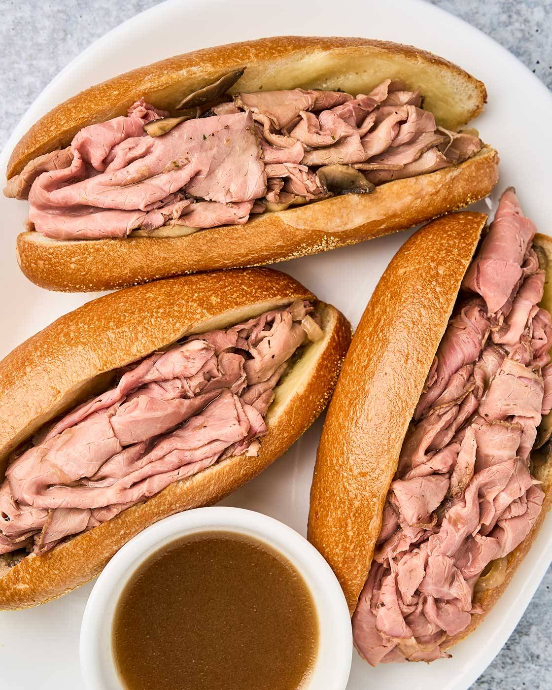 French dip sandwiches with deli roast beef on toasted rolls, served with a bowl of beef jus for dipping.