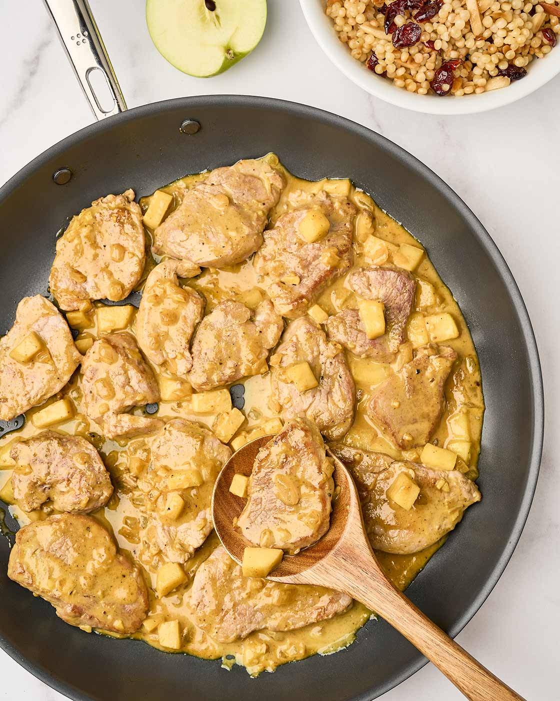 A skillet of pan seared pork tenderloin medallions and chunks of sautéed apple in a mild, creamy curry sauce.