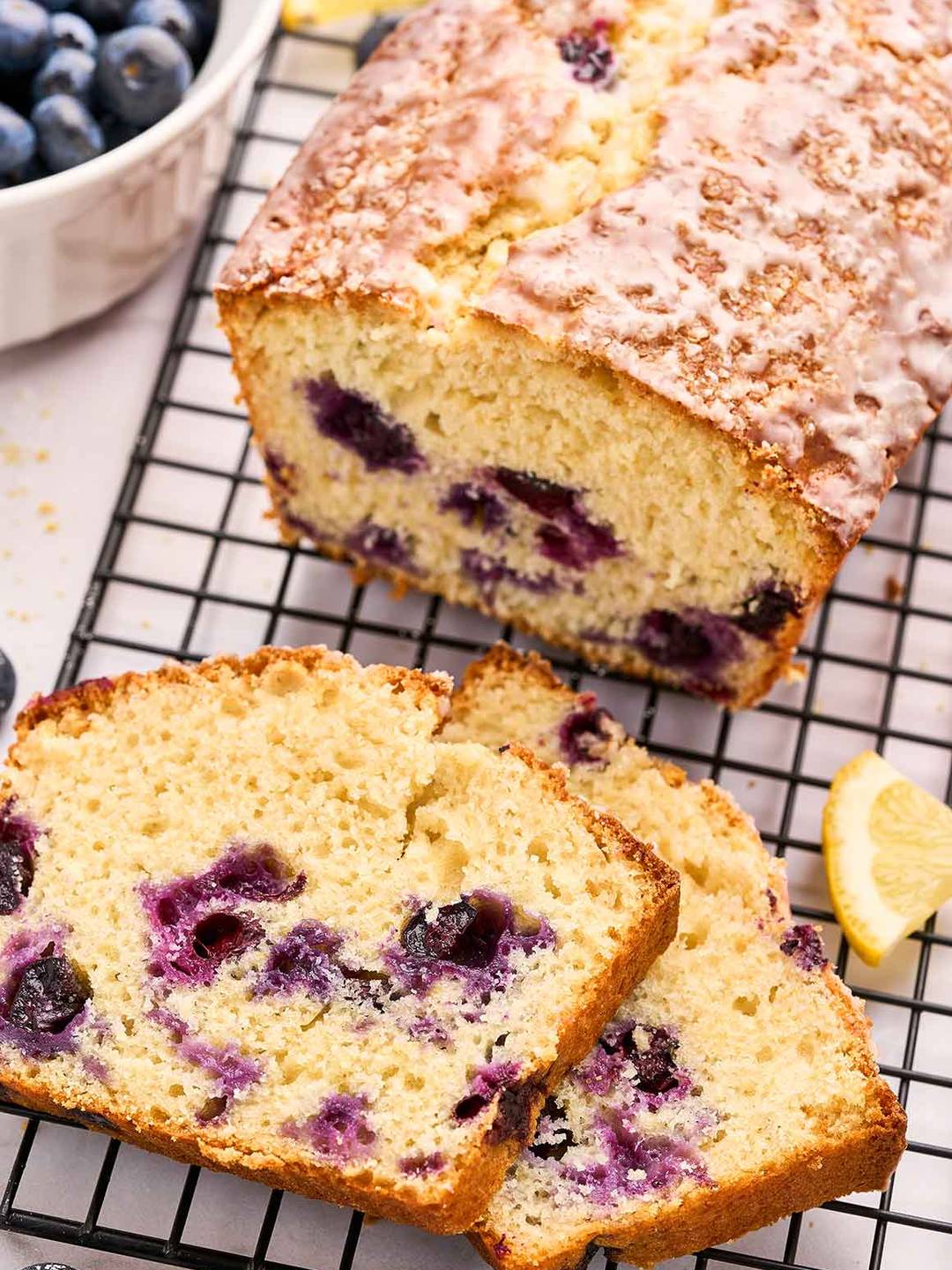 A partially sliced lemon and blueberry loaf cake on a black wire cooling rack.