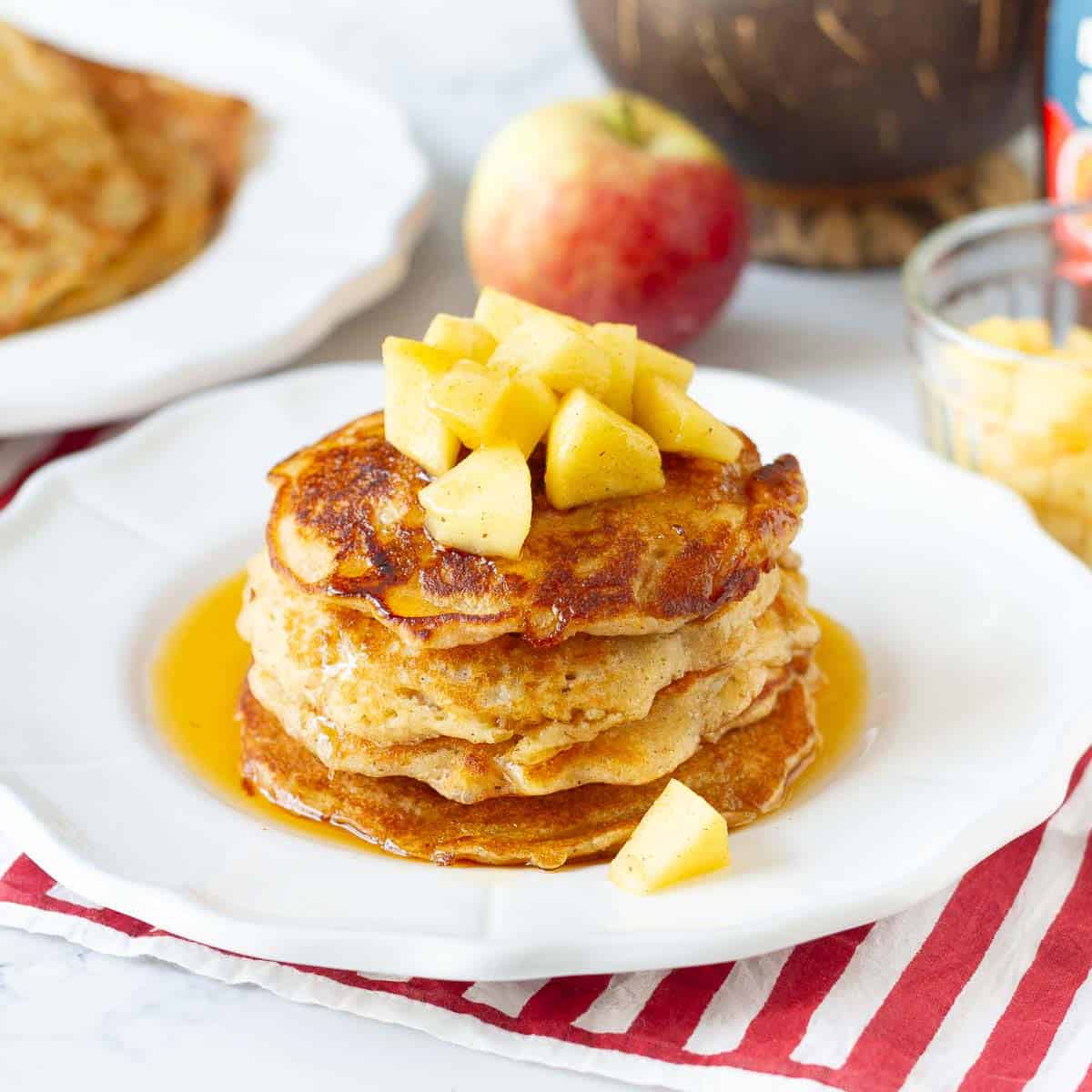 A stack of apple pancakes on a plate topped with apples.