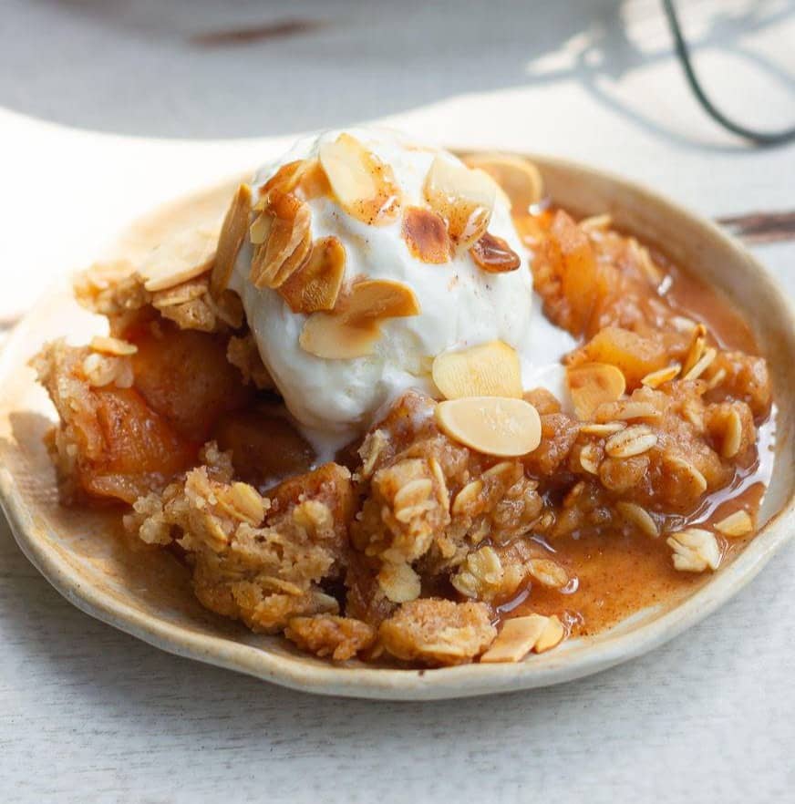 Apple crisp in a plate topped with vanilla ice cream.