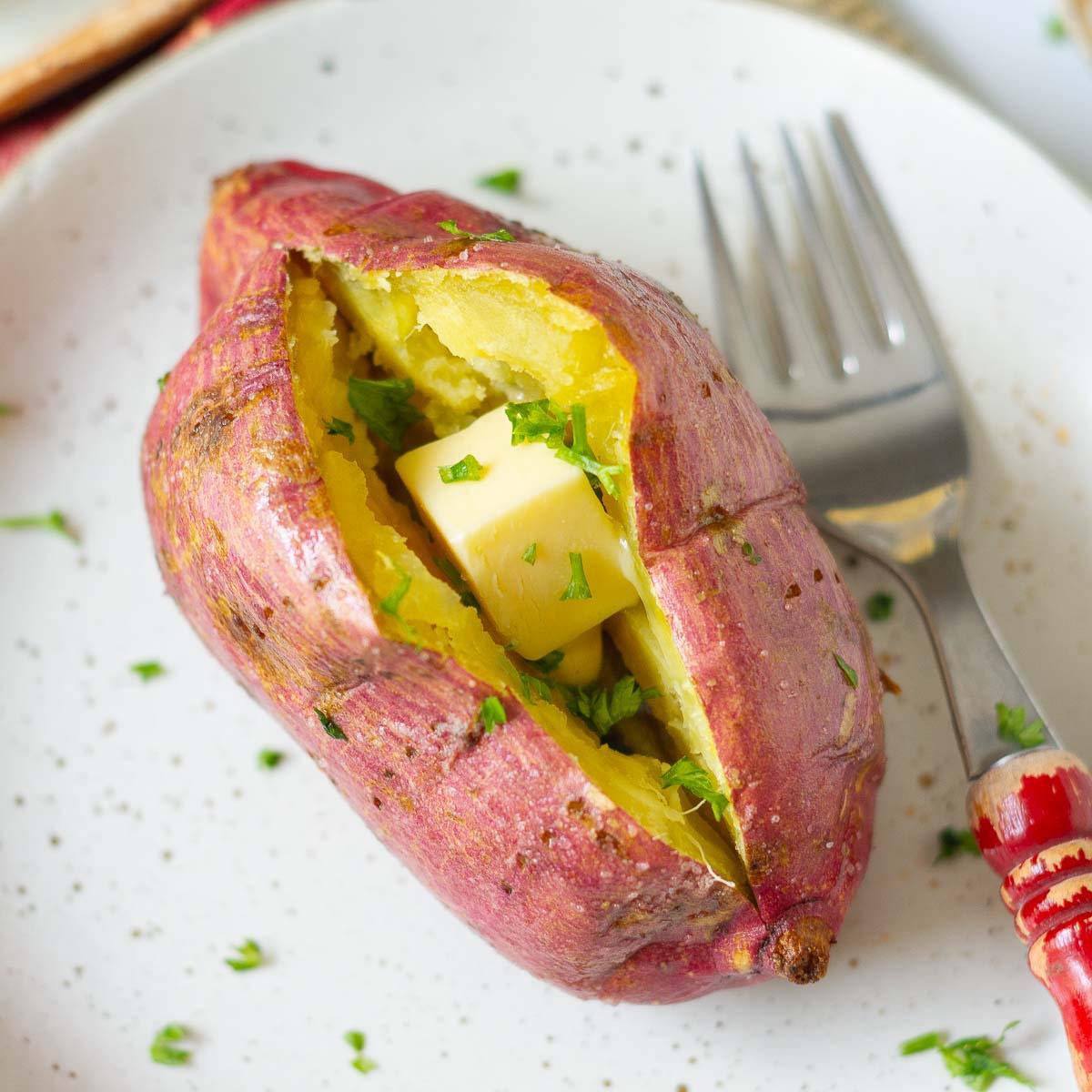 Baked sweet potato with butter and parsley with a fork on the side.
