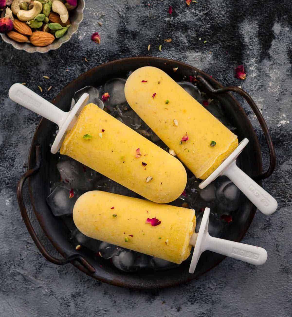 3 popsicles on a black plate filled with ice.