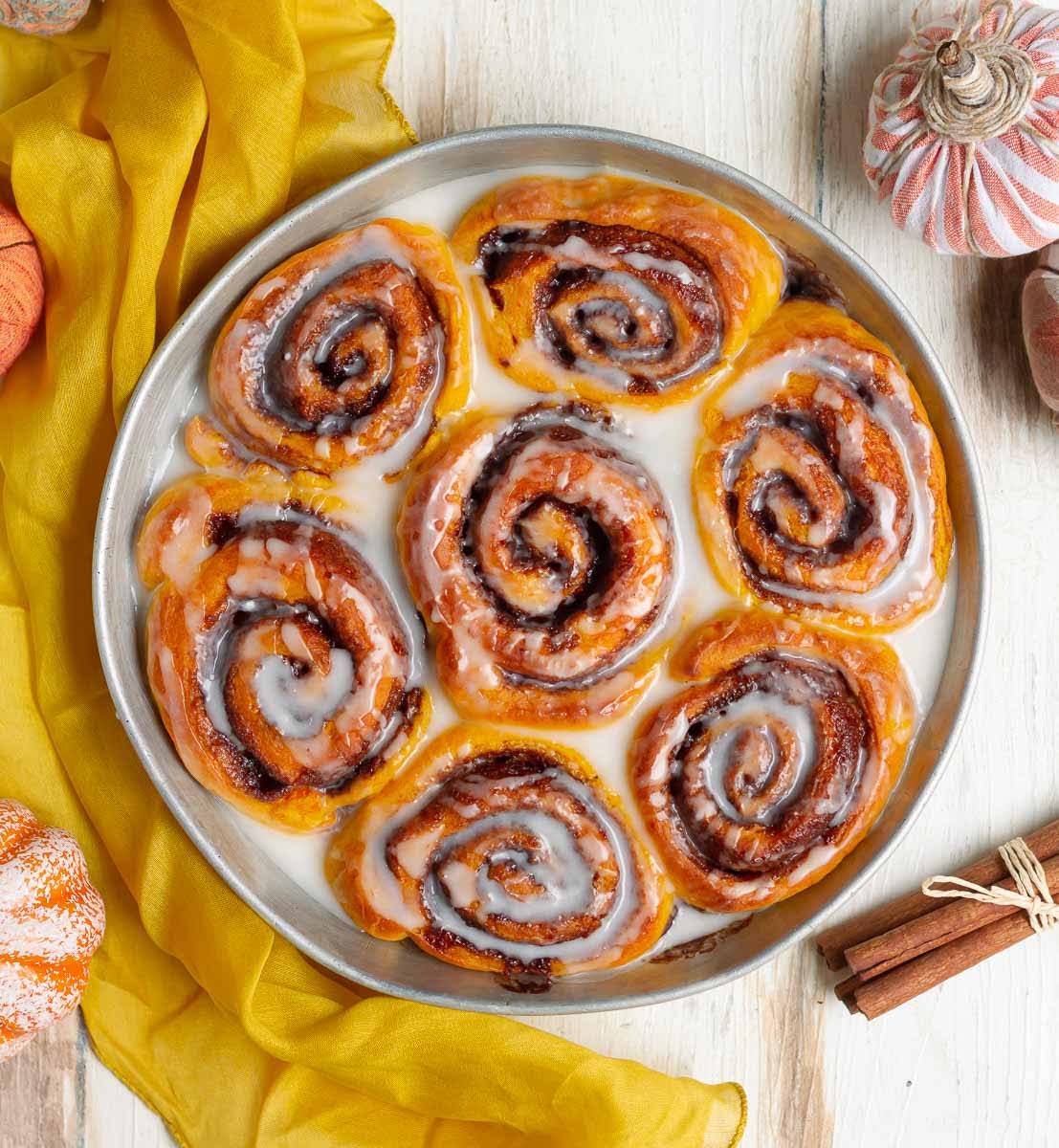 Pumpkin cinnamon rools with glaze in a round baking pan.