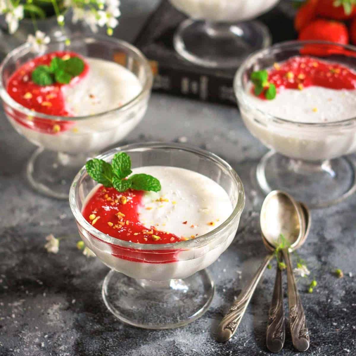 3 dessert glasses with coconut panna cotta topped with strawberry sauce.